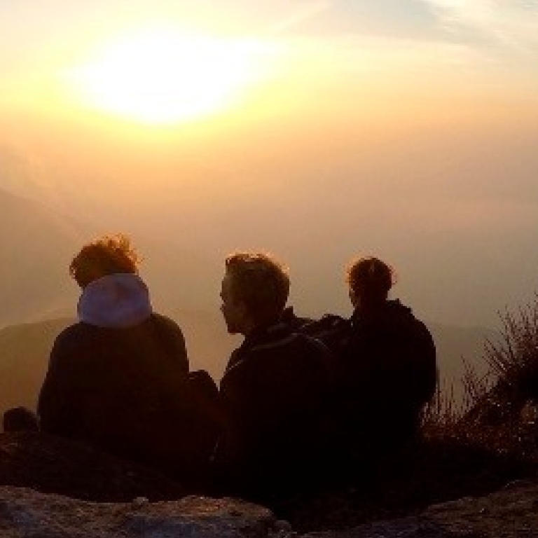 Tre människor på en kulle tittar ut över horisonten vid solnedgången