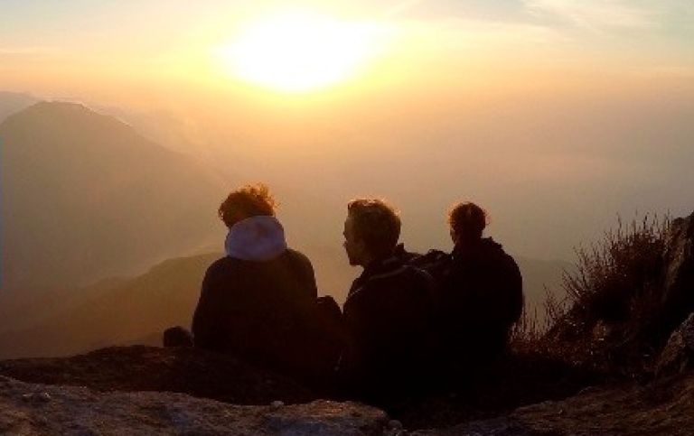 Three people on a hill looking out over the horizon at sunset